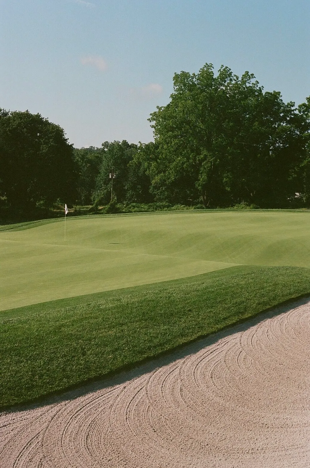 From the lip of a deep greenside bunker at Francis A. Byrne, looking across raked sand toward the pin and the green surface beyond