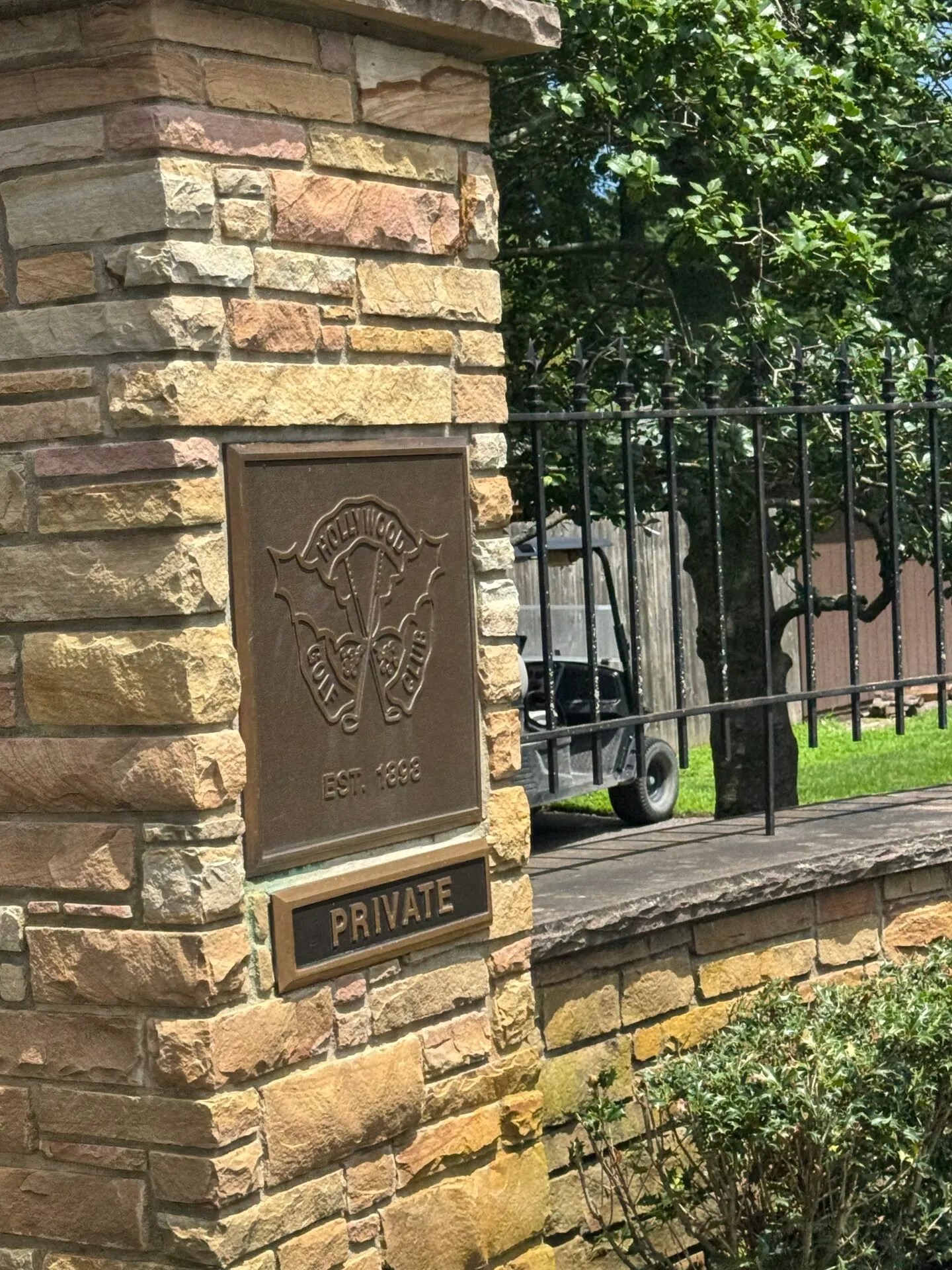 Bronze plaque on the stone gate pillar at Hollywood Golf Club showing the club crest with crossed clubs and holly berries, Est. 1898, with a PRIVATE sign below