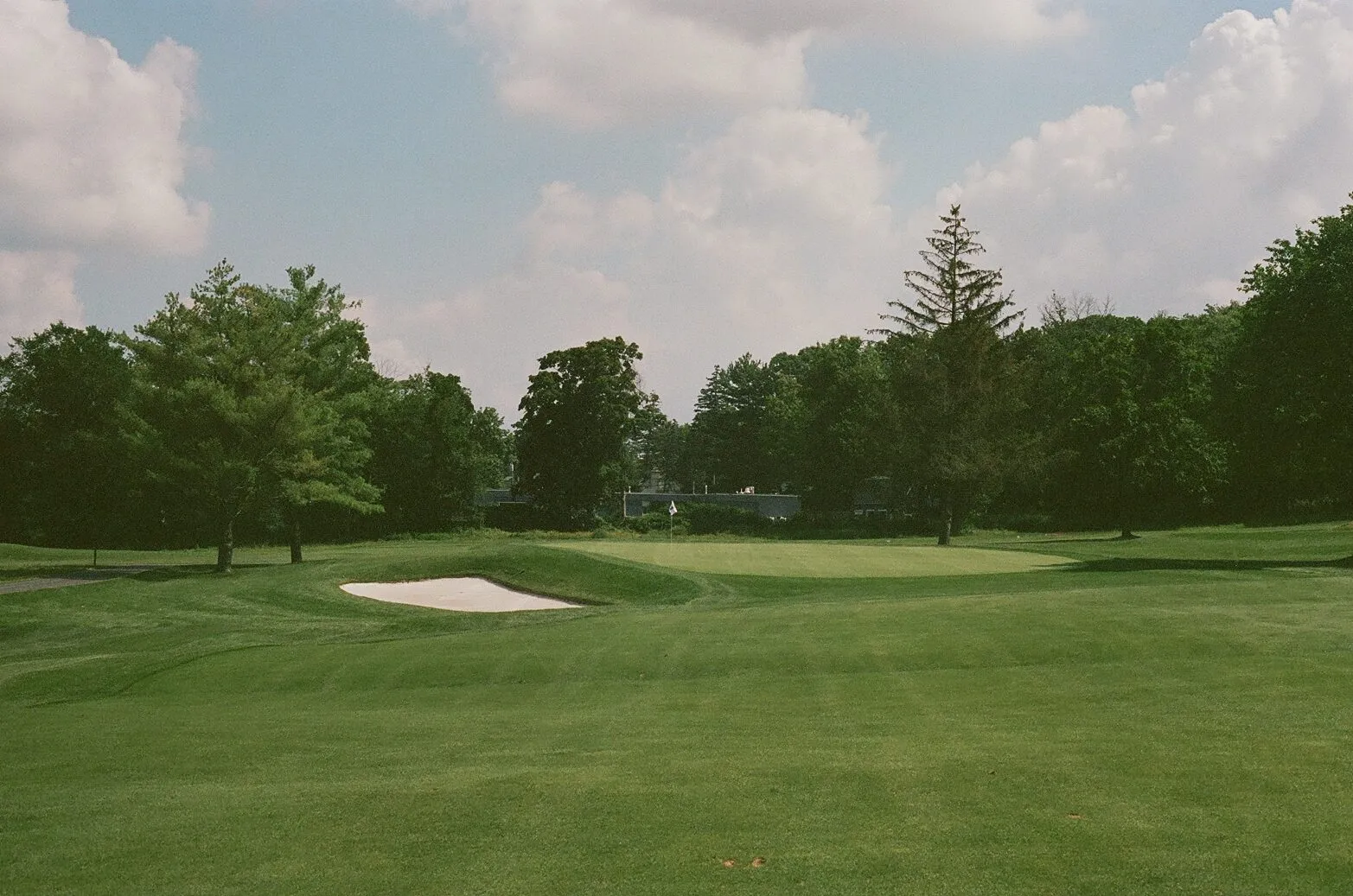 A green complex at Francis A. Byrne with a deep fronting bunker and the pin tucked behind, mature trees framing the background